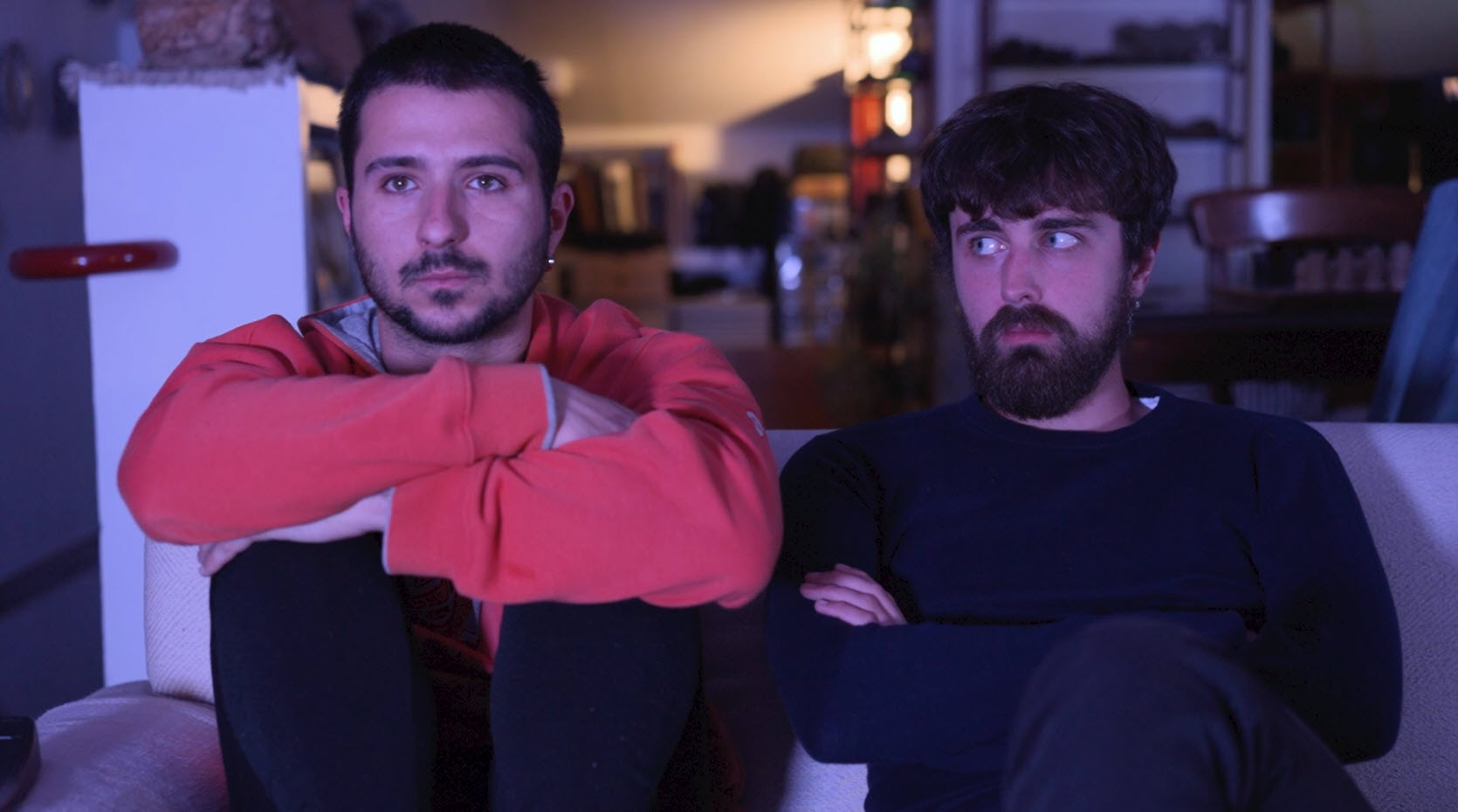 Dos hombres sentados en un sofá en una escena de interior con luz tenue