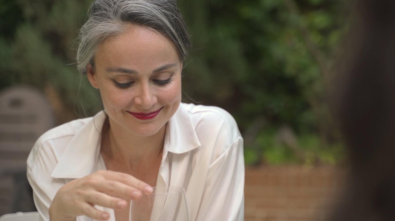 Mujer rubia sonriendo suavemente en exterior con fondo desenfocado